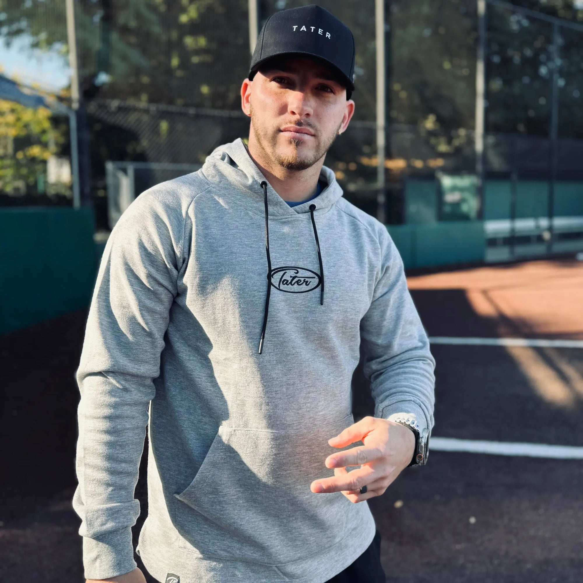 Stylish grey long-sleeve baseball lifestyle hoodie by Tater, featuring a minimalist black logo on the chest, a spacious front pocket, and black drawstrings, perfect for athletic leisure or casual wear.