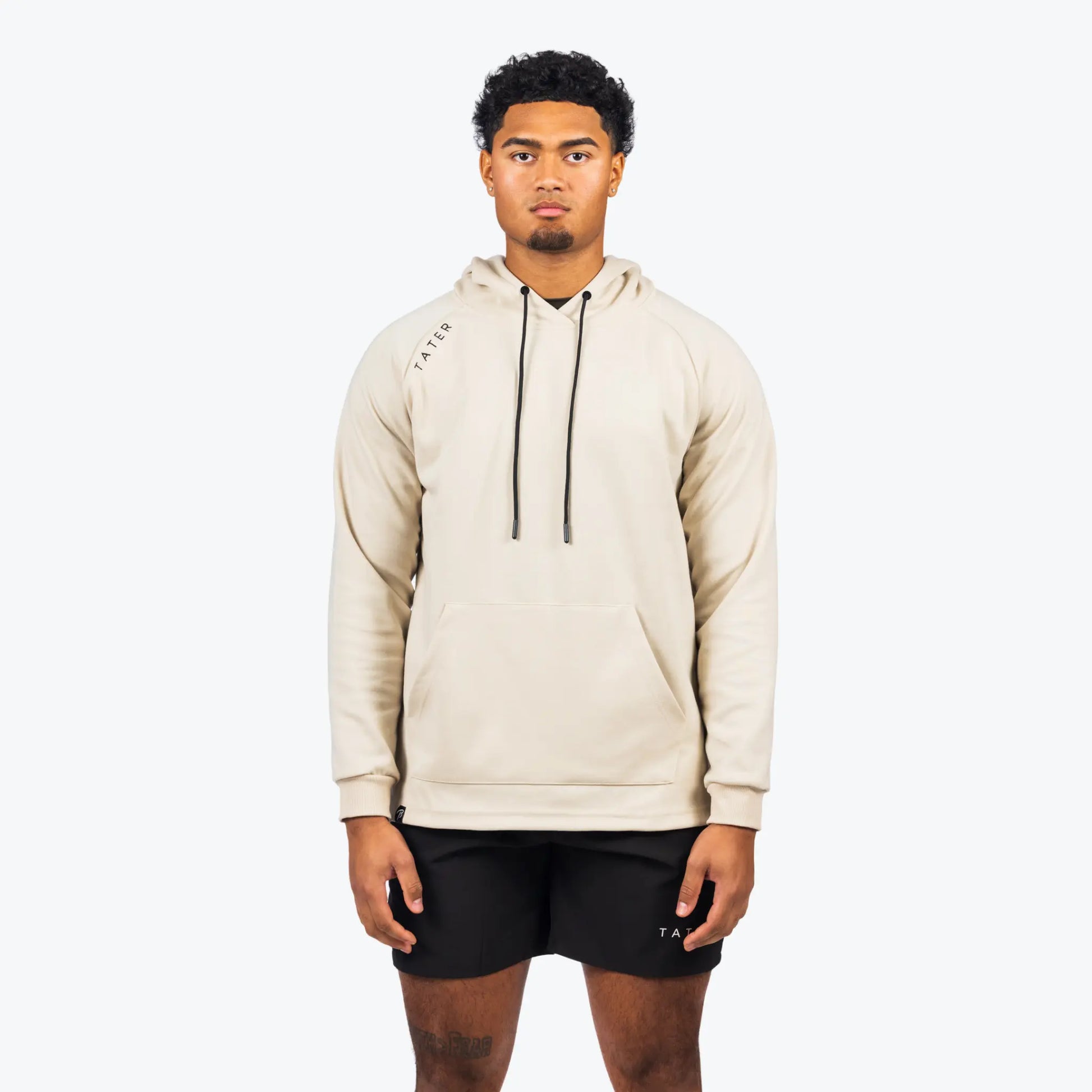 The uploaded image shows a model wearing a cream-colored professional baseball training hoodie with long sleeves, paired with black shorts, both adorned with the "TATER" logo. The hoodie, which is suitable for both sports training and casual wear, features a drawstring hood and a central front pocket. The style is modern and understated, emphasizing a practical and athletic lifestyle.