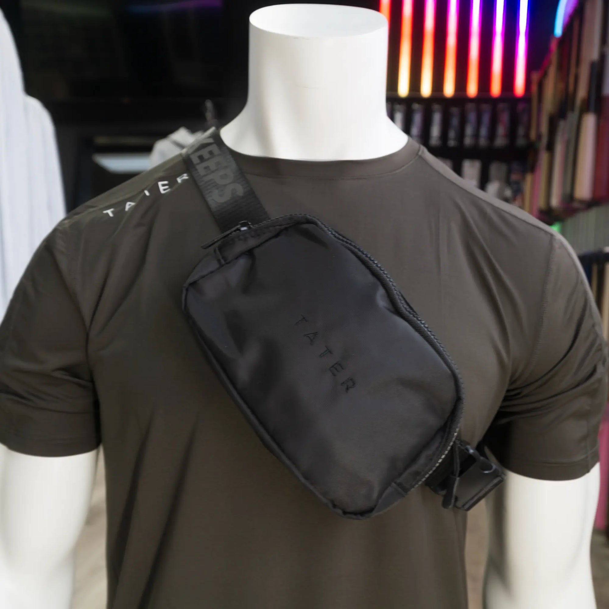 The image displays a black crossbody fanny pack with the "Tater" brand prominently embossed on the front. The strap bears a repeated slogan or message that appears to be part of the brand's design, enhancing the product's athletic appeal. The bag's compact size suggests functionality and convenience for carrying essentials, catering to an active lifestyle. 