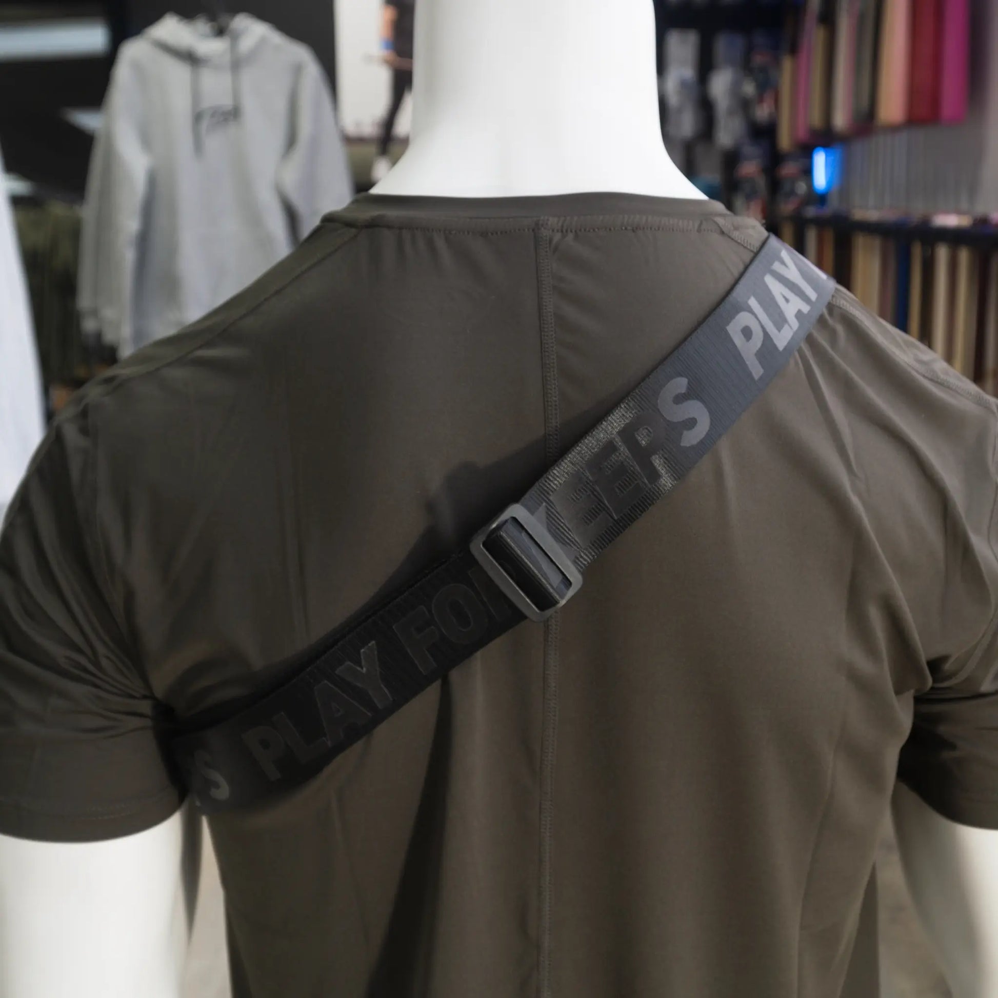 The photo shows a close-up of a strap with the words "PLAY FOR KEEPS" on a mannequin wearing a sporty shirt, showcasing the functional style of a Tater Baseball crossbody bag.