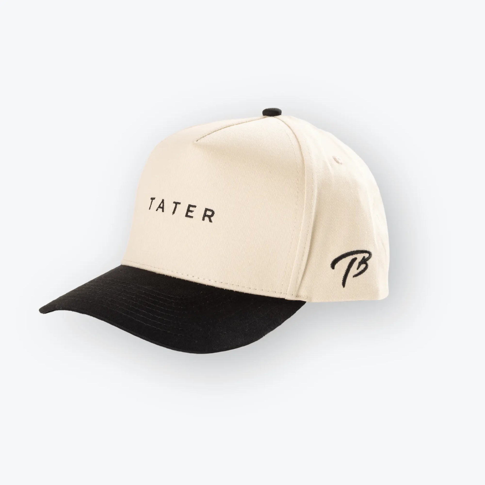 The image shows a tan and black snapback hat with the word "TATER" embroidered in black on the front. The Tater Baseball logo, a stylized "TB," is also embroidered on the side of the hat in black. The cap's design is simple yet stylish, aligning with the aesthetics of contemporary baseball lifestyle apparel.