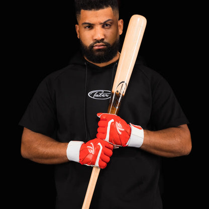 The image shows a focused baseball player, Aaron Bracho, in a black Tater Baseball shirt, confidently holding a Tater X12 Pro Maple bat over his shoulder. He's wearing striking red batting gloves with long straps, ready to step up to the plate.