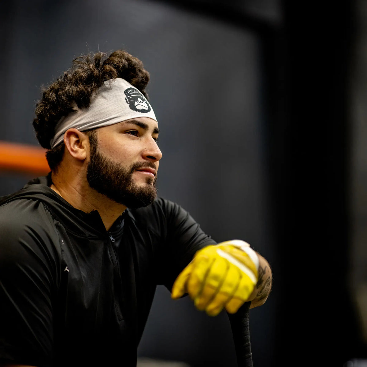 Baseball player in a focused stance wearing a Tater Kong headband and yellow batting gloves during a batting practice session, exuding confidence and concentration.