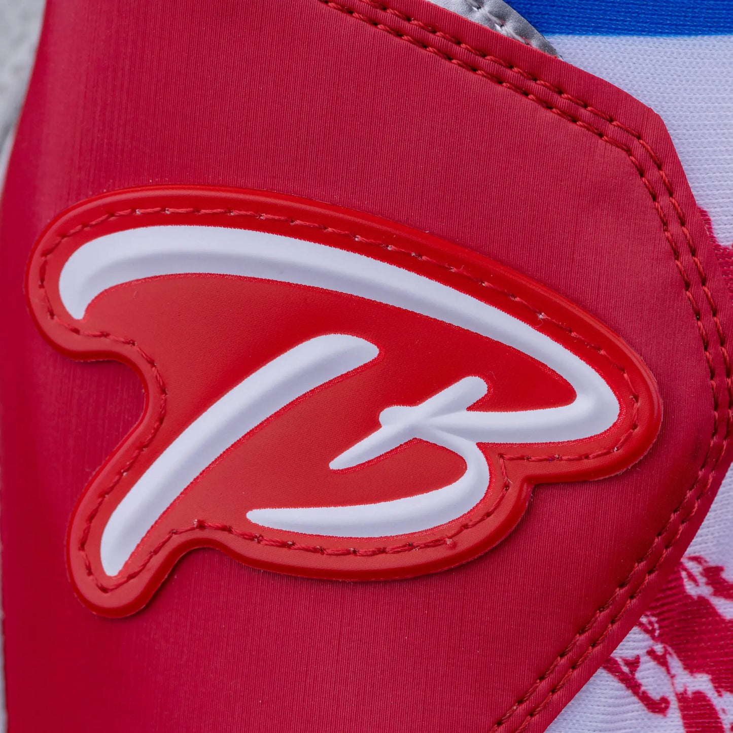 Close-up of the embossed 'TB' logo on red leather, part of Tater Baseball's premium batting gloves with a design inspired by the Puerto Rican flag.