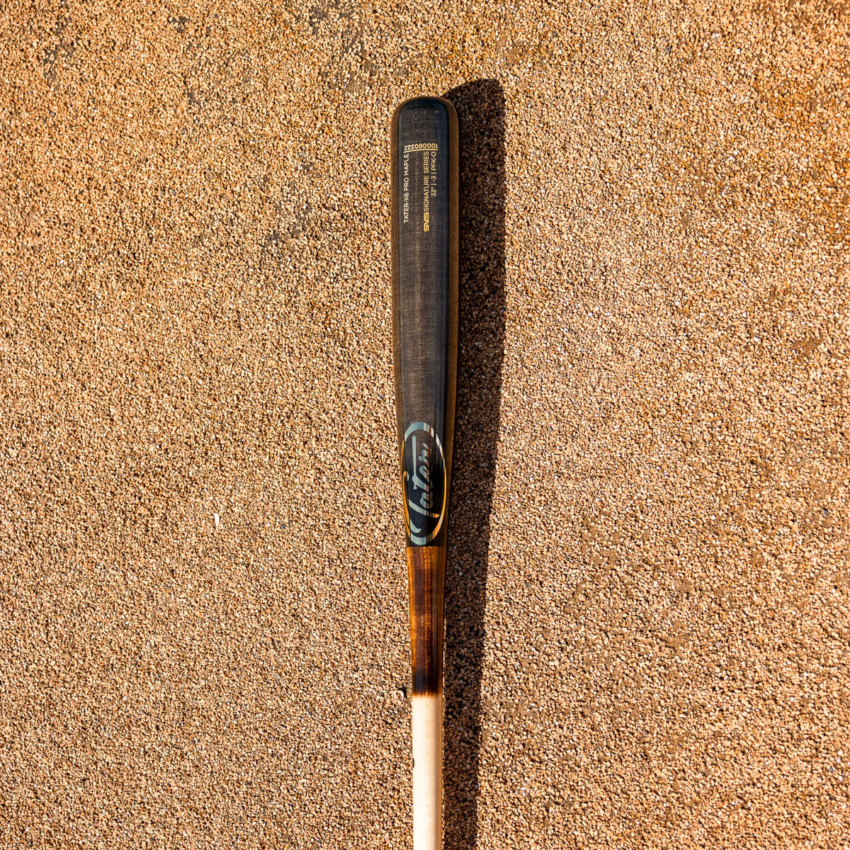 Tater Baseball high-quality custom maple wood bat lying on a sandy surface, showcasing the elegant black barrel and raw wood handle, ideal for travel baseball.