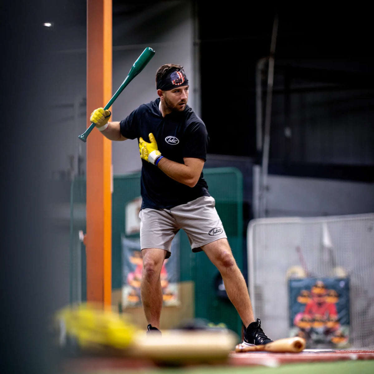 Focused baseball player engaged in one-hand batting drills with a Tater Baseball short training bat, wearing a Tater headband and batting gloves, exemplifying dedicated practice in an indoor facility.